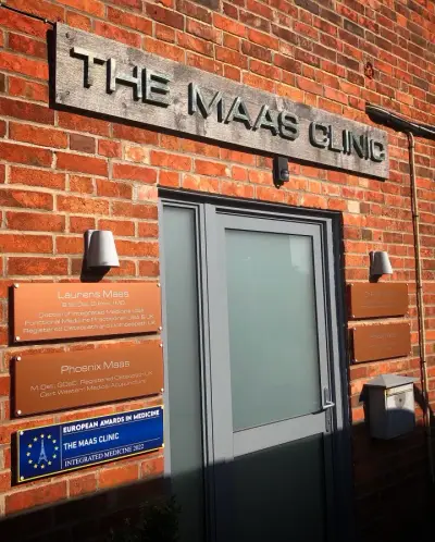 The Maas Clinic brushed-metal fascia sign and copper acrylic plaques on a brick wall beside the entrance door