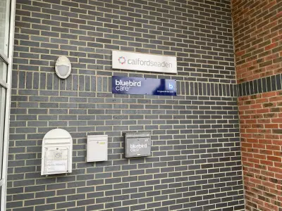 Exterior wall signs for calfordseaden and Bluebird Care mounted on grey brickwork above letterboxes