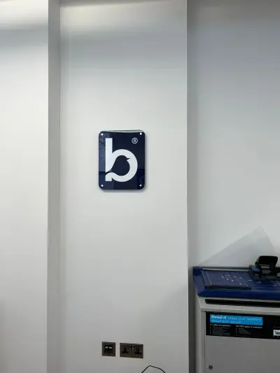 Navy acrylic Bluebird Care bird-logo plaque mounted on a white office wall