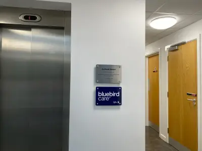 Calford House metal plaque and navy Bluebird Care Office acrylic sign on a hallway wall by a lift