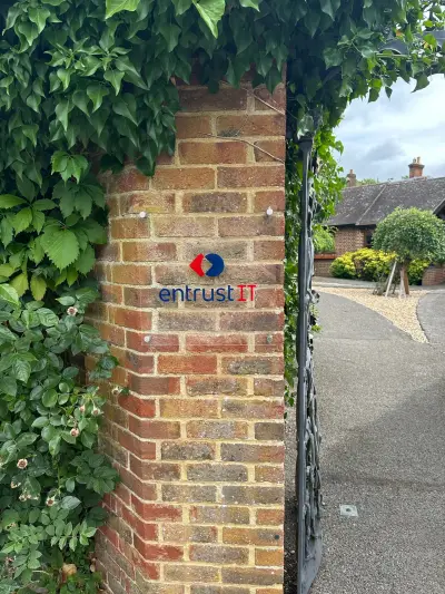 entrust IT logo sign on a clear acrylic panel fixed to an ivy-clad brick gate pillar
