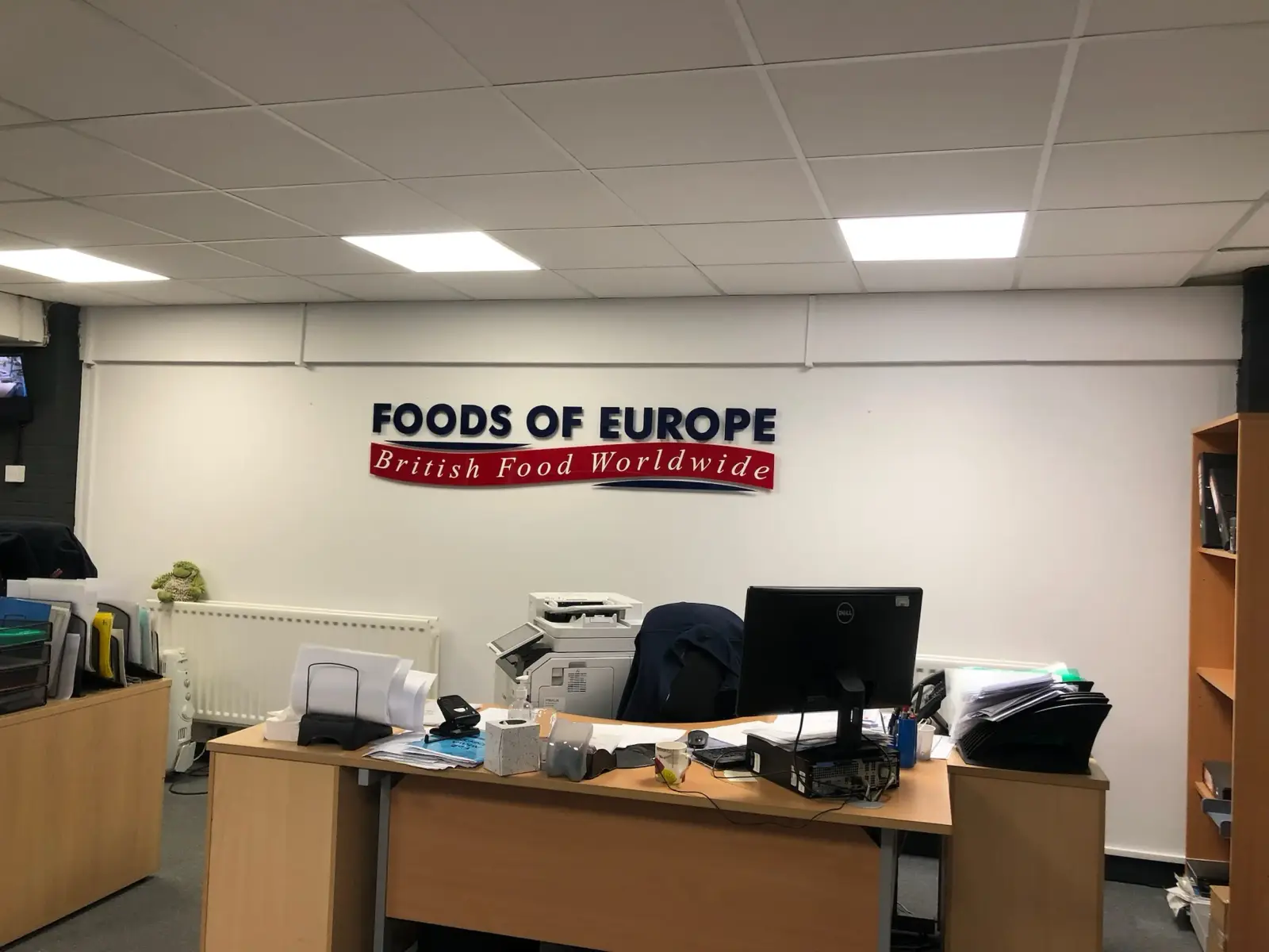 Acrylic wall-mounted sign reading 'Foods of Europe' with 'British Food Worldwide' subtitle in red and navy, installed in office