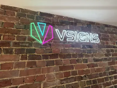 VSIGNS neon-effect LED sign with colourful V logo mounted on a red brick wall