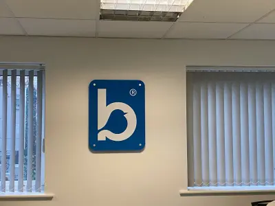 Blue acrylic Bluebird Care bird-logo plaque on an office wall between blind-covered windows