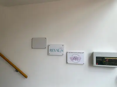 Acrylic Revalis and Beauty Hideaway office plaques on a stairwell wall beside a fire alarm panel