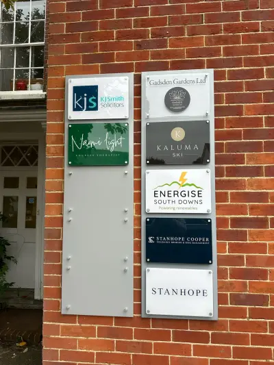Multi-tenant acrylic name plaques including KJ Smith Solicitors, Kaluma Ski and Stanhope on a brick wall
