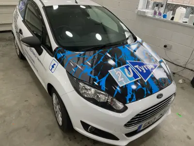 White Ford Fiesta van with blue splatter bonnet wrap and 2U Tyres logo, front three-quarter view