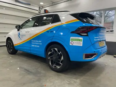 Blue and white Kia Sportage SUV, full wrap for Bluebird Care, front three-quarter view
