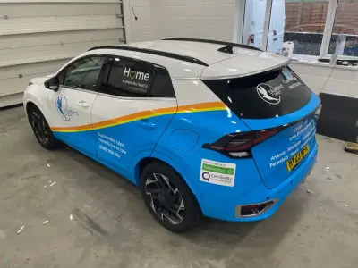 Blue and white Kia Sportage SUV, Bluebird Care full wrap, rear nearside three-quarter view