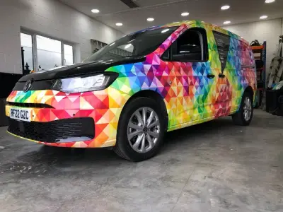 Floral Image rainbow VW Caddy van, full wrap, front three-quarter in trophy-lined workshop
