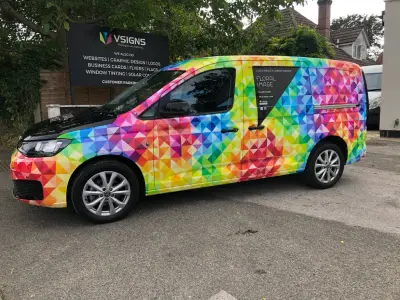 Floral Image rainbow VW Caddy van, full wrap, side view outdoors beside VSIGNS board