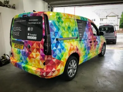 Side profile of Floral Image VW Caddy van in rainbow triangle full wrap, in workshop