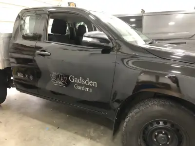 Nearside door of black Toyota Hilux pickup with Gadsden Gardens lotus-logo signwriting