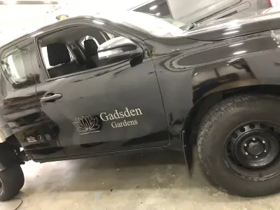 Offside door of black pickup with cut-vinyl Gadsden Gardens lotus logo and signwriting