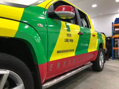 Driver side of Green Label PHEM pickup, green/yellow/red wrap reading Enhanced Care and web address