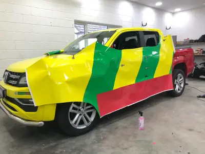 Green Label PHEM pickup mid-install with yellow, green and red wrap film draped over the body