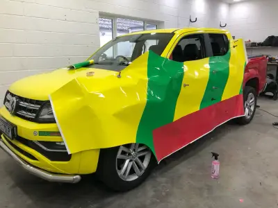 VW Amarok pickup during wrap install, yellow and green film loosely applied to the side