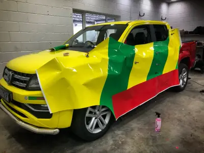 Yellow VW Amarok pickup part-way through wrap install, green and red film hanging over the door