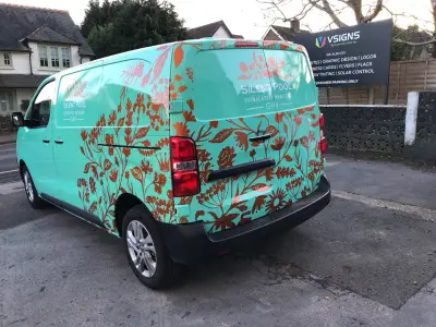 Turquoise Silent Pool Gin van with floral wrap parked by VSIGNS pavement sign, rear view