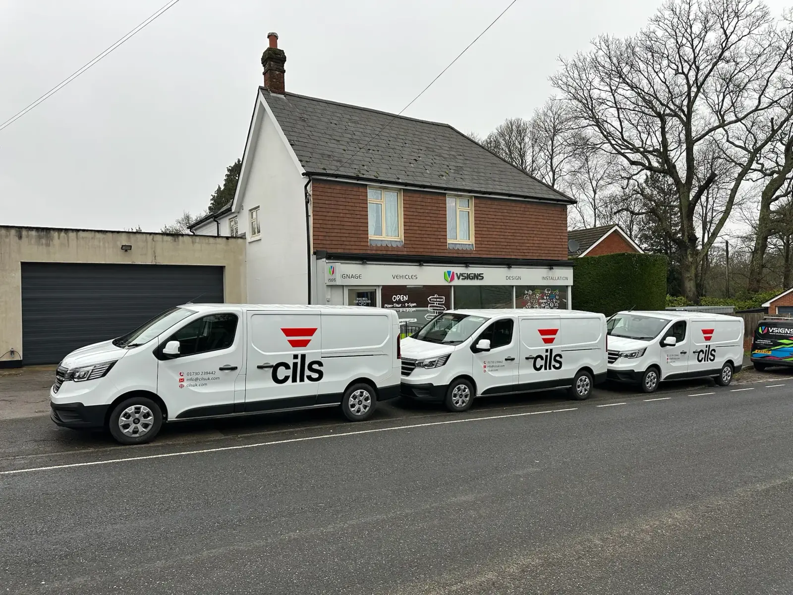 Three white Renault vans with red and black 'cils' branding and logo parked in front of a brick commercial building