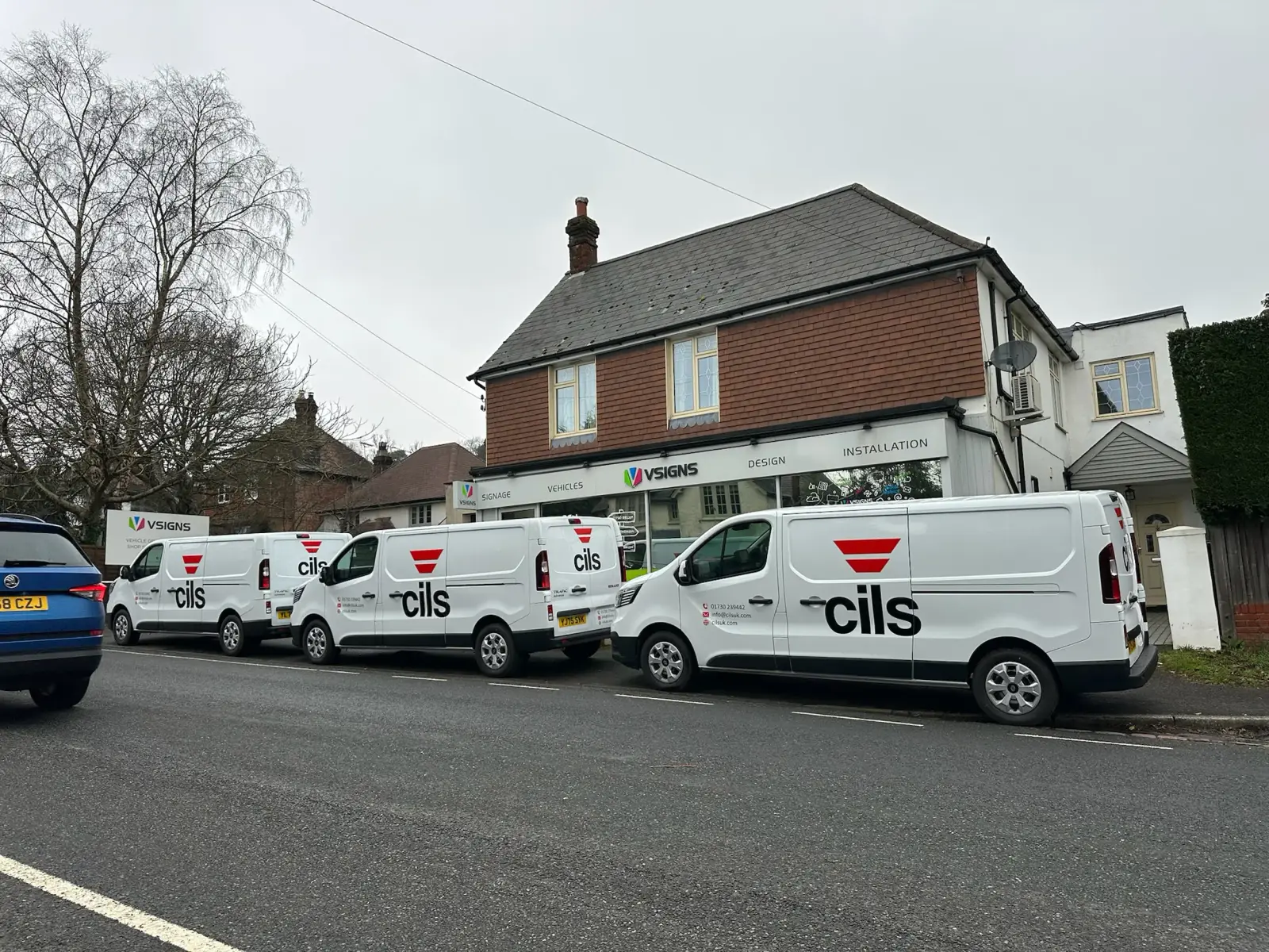 Three cils-branded white Renault Trafic fleet vans with matching vinyl graphics outside the V Signs shopfront