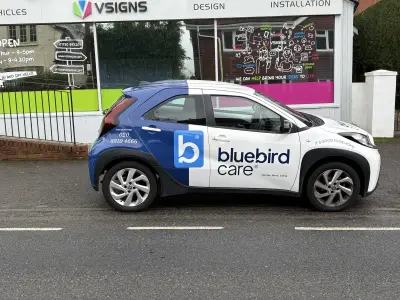 White and blue Toyota Aygo X wrapped for Bluebird Care Harrow, parked outside the V Signs shopfront