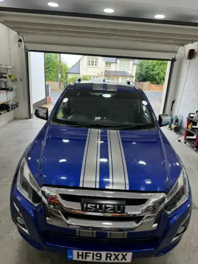 Blue Isuzu D-Max pickup with silver racing stripes, front view in workshop