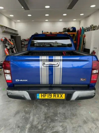 Rear of blue Isuzu D-Max pickup with silver twin racing stripes down the tailgate