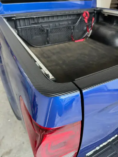 Carbon-fibre vinyl trim on the load-bed rail of a blue Isuzu D-Max pickup