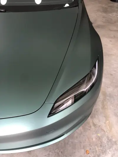 Bonnet and headlight of a Tesla Model S wrapped in matt metallic pine green colour-change vinyl