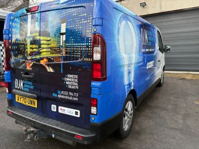 Blue van fully wrapped for DJK Electrical Contractors with lightbulb and cityscape graphics, rear quarter