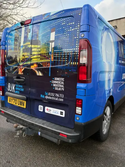 Blue DJK Electrical Contractors van with cityscape and lightbulb full wrap, rear quarter