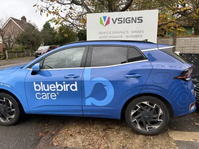 Blue Kia Sportage side with Bluebird Care full wrap parked by V Signs forecourt sign