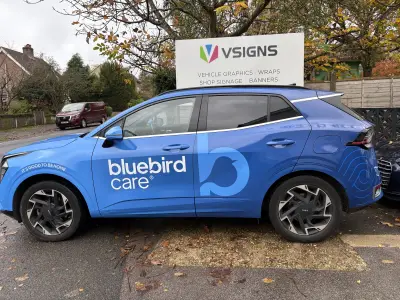 Blue Kia Sportage side, Bluebird Care full wrap, in front of V Signs company board