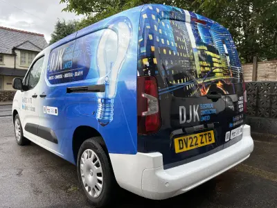 Rear quarter of DJK Electrical compact van with lit skyline and lightbulb full wrap