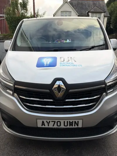 Front of silver Renault Trafic van with DJK Electrical Contractors bonnet logo and lightbulb