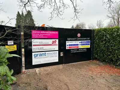 Black construction hoarding panels with contractor and site safety signs at a site gate