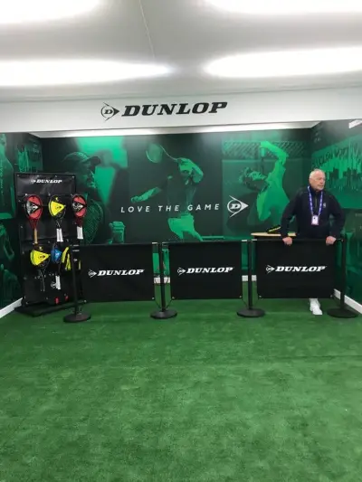 Dunlop tennis stand with green 'Love the Game' printed backdrop, fascia sign and barrier banners