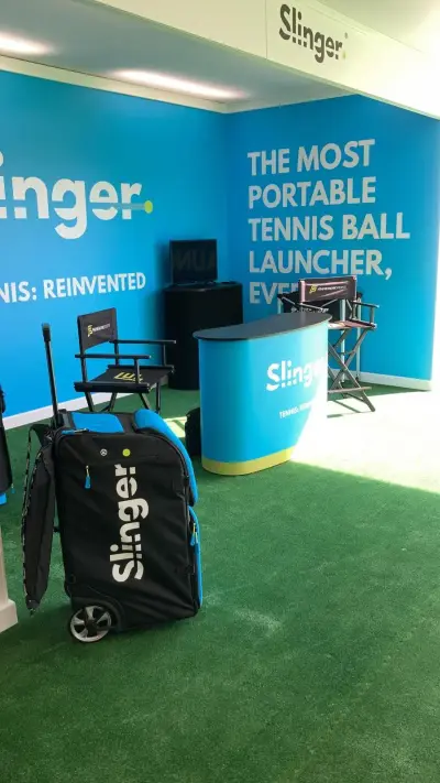 Slinger tennis stand with blue 'most portable tennis ball launcher' wall graphics and branded counter