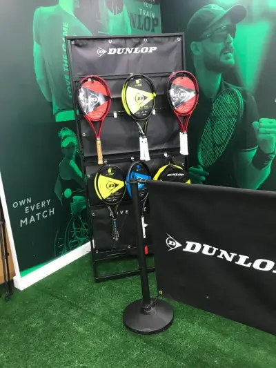 Dunlop tennis racket display against green printed player backdrop with branded barrier banner