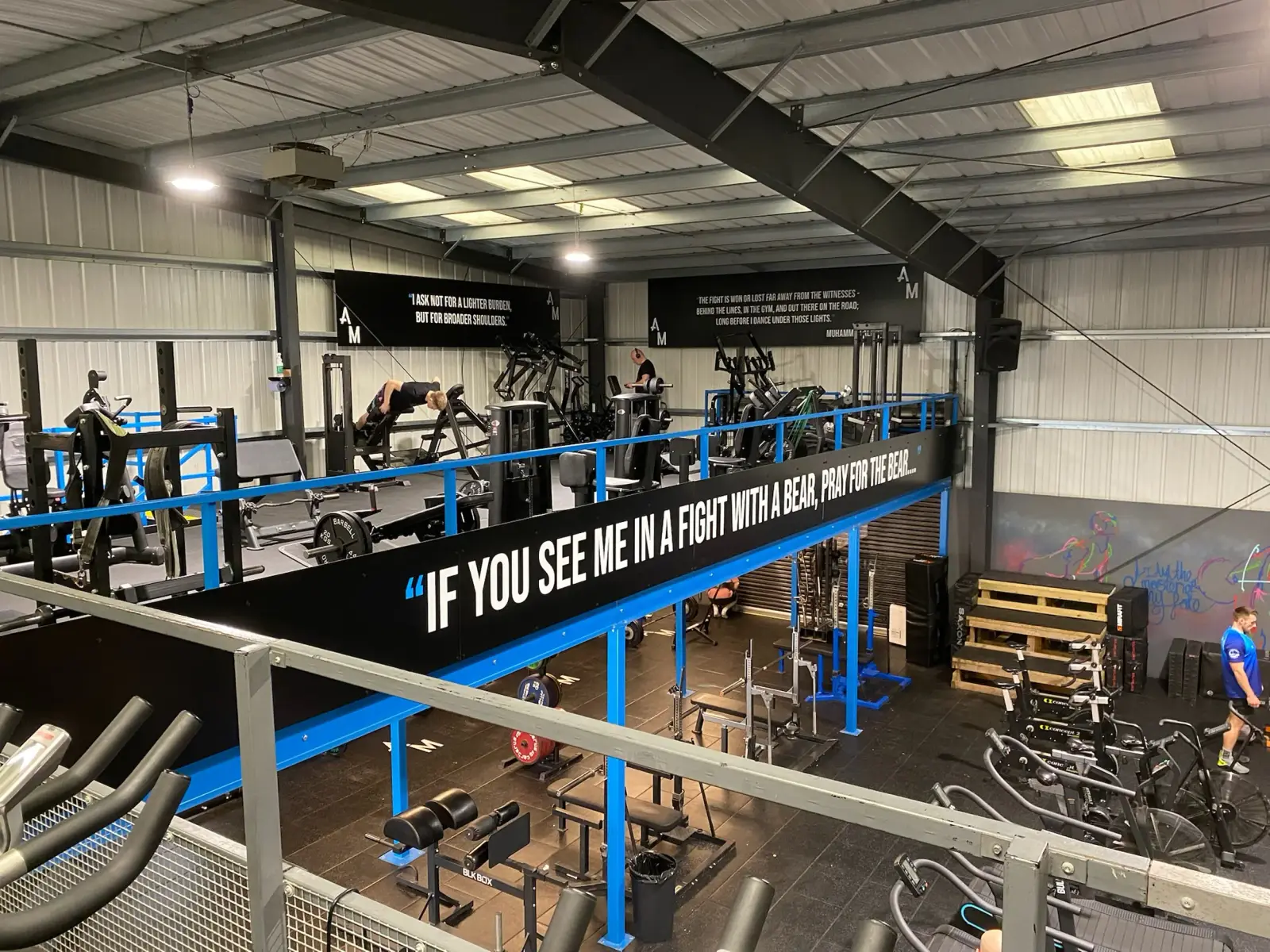 Large-format black and blue vinyl banner with white text mounted on blue metal railings in a gym interior