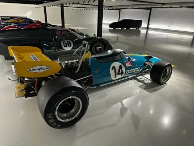 Teal and yellow classic F1 car number 14 with exposed engine and yellow rear wing, rear-quarter view
