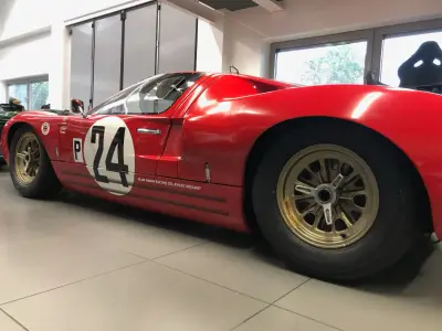 Red Ford GT40 side view with black P24 race number graphic and gold wheels in showroom