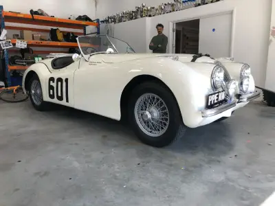 Cream Jaguar XK120 roadster race car with black 601 door-number decal, in workshop