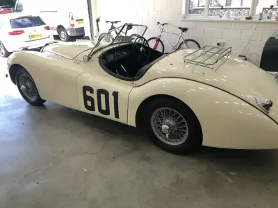 Cream Jaguar XK120 open two-seater with 601 race-number decal, side profile in garage