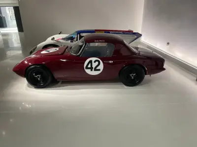 Maroon Lotus Elan 26R coupe with black 42 roundel and Jackie Oliver name, side view in showroom