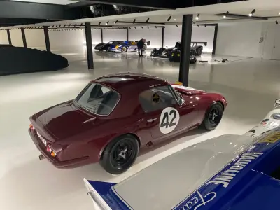 Maroon Lotus Elan 26R coupe number 42, rear three-quarter view among race cars in showroom