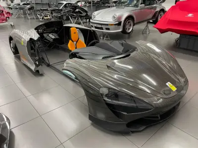 Disassembled silver pinstripe-wrapped McLaren Speedtail with orange seat in showroom