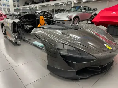 Grey pinstripe-wrapped McLaren Speedtail bodywork in showroom, Porsche 911 behind