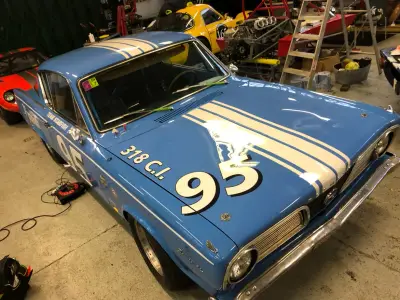 Blue Plymouth Barracuda race car with number 95 and 318 C.I. front three-quarter in workshop